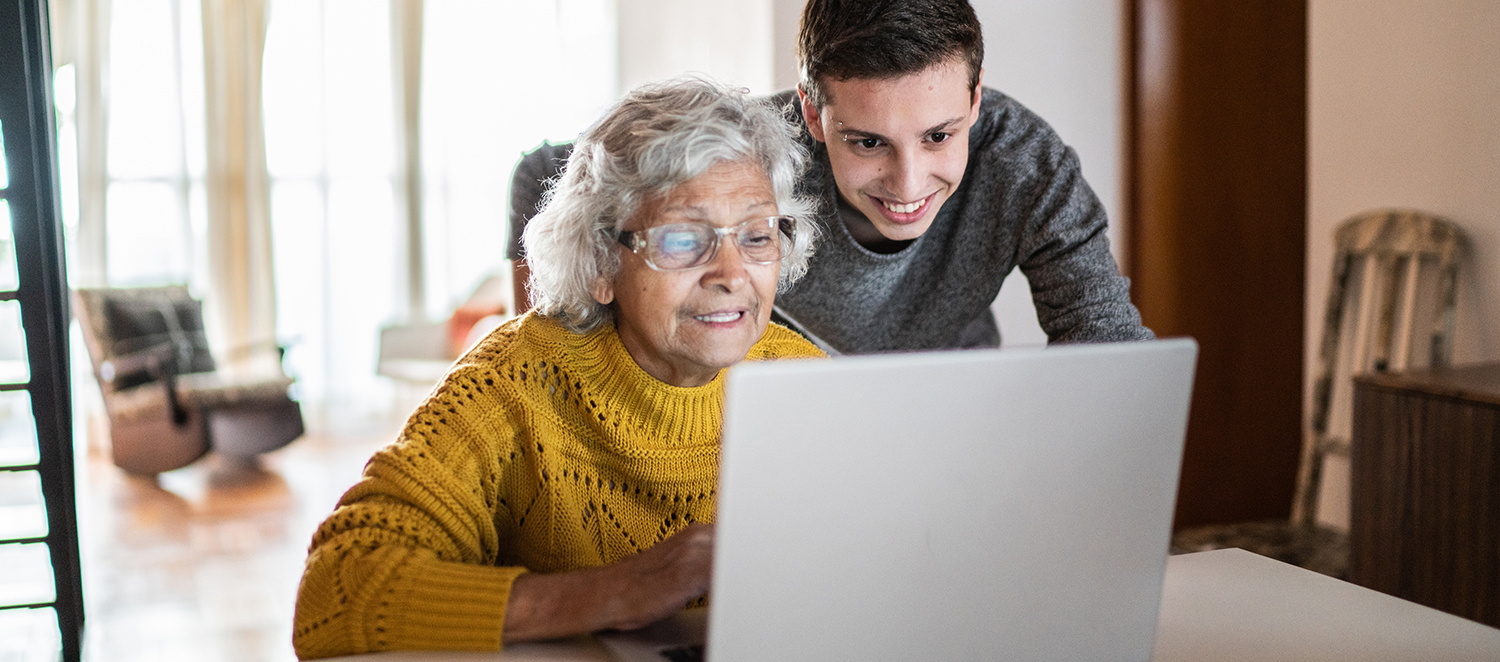 Eine ältere Frau und ein junger Mann schauen gemeinsam auf einen Laptop