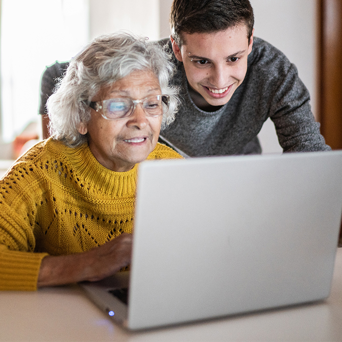 Eine ältere Frau und ein junger Mann schauen gemeinsam auf einen Laptop