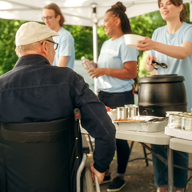  Ein Mann mittleren Alters mit Behinderungen im Rollstuhl an einer Lebensmittelausgabe von Freiwilligen. 